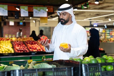 رجل إماراتي يتسوق الخضروات الطازجة في السوبر ماركت