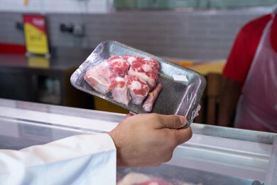 رجل إماراتي يمسك طبق لحم طازج في السوبر ماركت