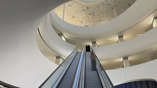 صورة من الداخل لسيدة تصعد على درج مركز اثراء، 5 أكتوبر 2025، مكان للقراء ومحبي العلم والكتب والمعرفة، أكبر المكتبات العامة في السعوديه، مركز الملك عبد العزيز الثقافي العالمي (إثراء) في مدينة الظهران في المملكة العربية السعودية, كتب و روايات وقصص مرتبة في الرفوف.