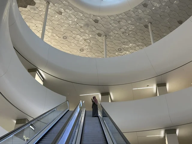 صورة من الداخل لسيدة تصعد على درج مركز اثراء، 5 أكتوبر 2025، مكان للقراء ومحبي العلم والكتب والمعرفة، أكبر المكتبات العامة في السعوديه، مركز الملك عبد العزيز الثقافي العالمي (إثراء) في مدينة الظهران في المملكة العربية السعودية, كتب و روايات وقصص مرتبة في الرفوف.