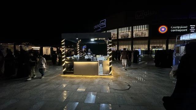 مبنى في الخلفية مضاء بنوافذ كبيرة، فعالية تكوة في جدة في المملكة العربية السعودية  17 يناير 2026،  تجربة شتوية تجمع بين الترفيه، التسوق، والمطاعم، تشمل الفعالية عرض موسيقي حي وفرق استعراضية متجولة،  مخصصة لجميع أفراد العائلة