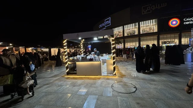 مبنى في الخلفية مضاء بنوافذ كبيرة، فعالية تكوة في جدة في المملكة العربية السعودية  17 يناير 2026،  تجربة شتوية تجمع بين الترفيه، التسوق، والمطاعم، تشمل الفعالية عرض موسيقي حي وفرق استعراضية متجولة،  مخصصة لجميع أفراد العائلة