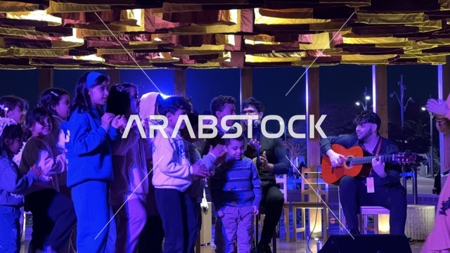 تفاعل الاولاد مع فنان يقدم عرض موسيقي في فعالية شارع أسبانيا في مركز الملك عبدالعزيز الثقافي العالمي "إثراء" بمدينة الظهران في المنطقة الشرقية، المملكة العربية السعودية، يوم 11 من أكتوبر 2025، تجربة ثقافية وترفيهية ، رقصات فلامنكو وفعاليات تفاعلية، مطاعم ومقاهي بطابع اسباني، أنشطة مناسبة العائلات والأطفال، أجواء احتفالية نابضة بالحياة.