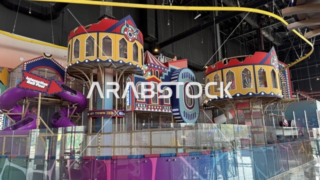 Activities and entertainment games at the Yo Walk complex in Jeddah, Saudi Arabia, an open walkway with a modern design, international and local restaurants and cafes, a comprehensive urban destination for walking, entertainment, and shopping, diverse brand names, the exterior design of the Sinomi Mall building, outdoor seating and social spaces, vibrant family and youth atmosphere.