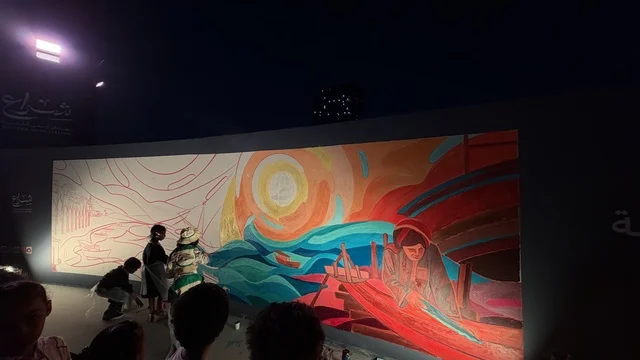A vibrant mural on display, the Wooden Ships Festival on the Al-Hamra Beach in Jeddah, Saudi Arabia from January 12 to 16, 2026, showcases stages of traditional shipbuilding, tools and materials used, maritime heritage and coastal identity, interactive activities, and cultural performances.
