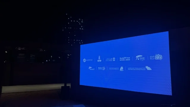 شاشة عرض كبيرة مضاءة باللون الأزرق، عروض لمراحل بناء السفن التقليدية والأدوات والمواد المستخدمة، مهرجان السفن الخشبية على شاطئ الحمراء بجدة في المملكة العربية السعودية 12 إلى 16 يناير 2026، التراث البحري، الأنشطة التفاعلية والعروض الثقافية