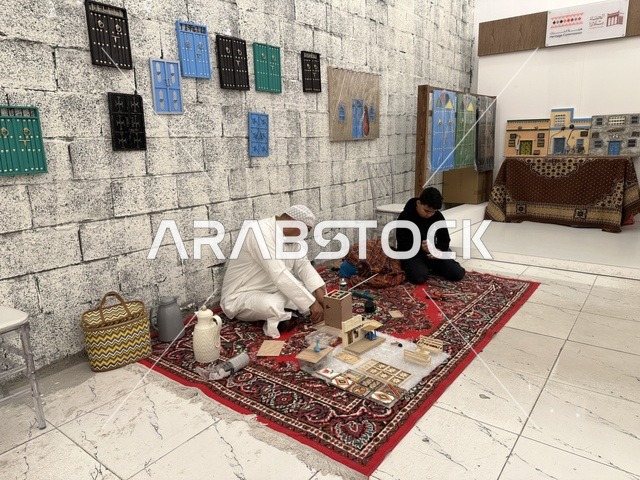 شخصان جالسان على سجادة حمراء يعملان على مجسمات، تجربة تسوق مابين عبق الزمان وأصالة المكان، فعالية حياة زمان في المنطقة الشرقية الدمام خلال شهر يناير 2026 في المملكة العربية السعودية، ملامح الماضي وحياة القديمة من خلال أجواء تراثية