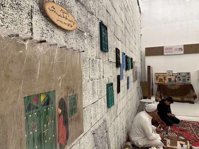 شخصان جالسان على سجادة حمراء يعملان على مجسمات، تجربة تسوق مابين عبق الزمان وأصالة المكان، فعالية حياة زمان في المنطقة الشرقية الدمام خلال شهر يناير 2026 في المملكة العربية السعودية، ملامح الماضي وحياة القديمة من خلال أجواء تراثية