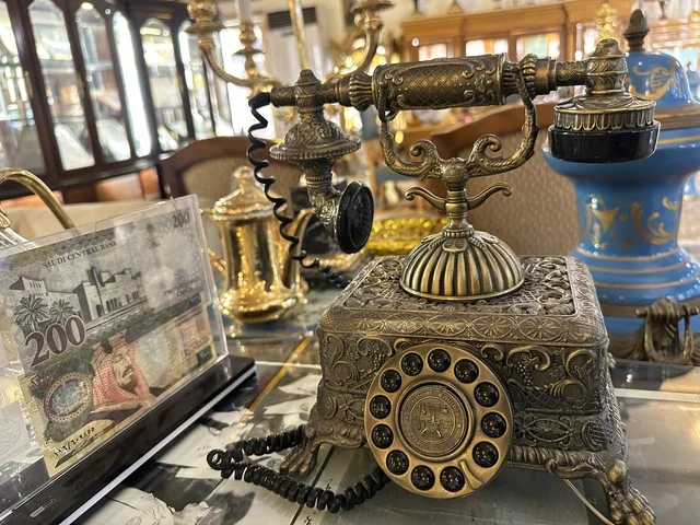 A decorative brass rotary phone at the Al-Falwah and Al-Jawhara Museum in the Al-Nuzha neighborhood of Dammam, Eastern Province, Saudi Arabia, on February 21, 2018, a distinctive educational and tourist destination, Saudi heritage, classic cars, a heritage and cultural landmark showcasing the history of traditional clothing and jewelry, documentation of handicrafts and Saudi identity, Islamic art.