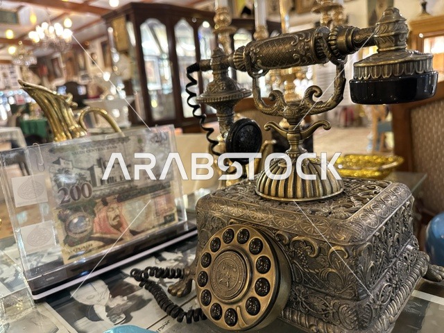 A decorative brass rotary phone at the Al-Falwah and Al-Jawhara Museum in the Al-Nuzha neighborhood of Dammam, Eastern Province, Saudi Arabia, on February 21, 2018, a distinctive educational and tourist destination, Saudi heritage, classic cars, a heritage and cultural landmark showcasing the history of traditional clothing and jewelry, documentation of handicrafts and Saudi identity, Islamic art.
