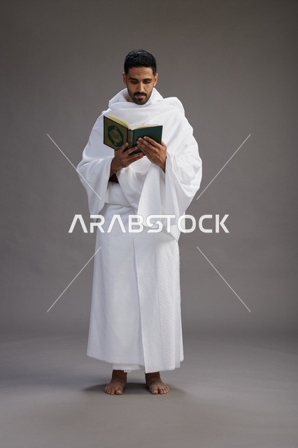 بورتريه لرجل سعودي بملابس الإحرام يقرأ القرآن أثناء الحج,  الجسم بالطول الكامل ,خلفيه رماديه
