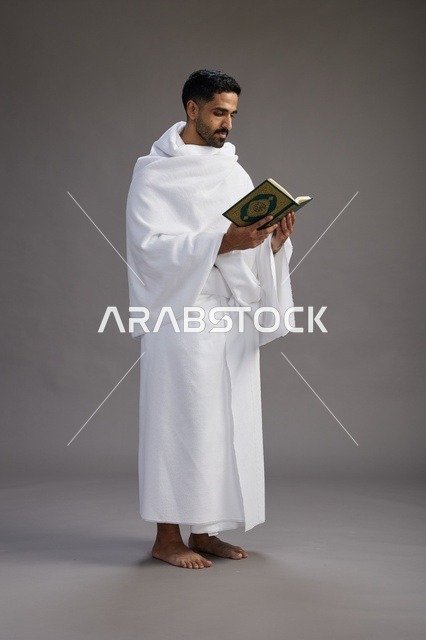 بورتريه لرجل سعودي بملابس الإحرام يقرأ القرآن أثناء الحج,  الجسم بالطول الكامل ,خلفيه رماديه