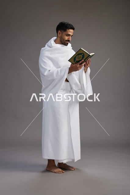 بورتريه لرجل سعودي بملابس الإحرام يقرأ القرآن أثناء الحج,  الجسم بالطول الكامل ,خلفيه رماديه