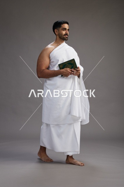 بورتريه لرجل سعودي بملابس الإحرام يقرأ القرآن أثناء الحج,  الجسم بالطول الكامل ,خلفيه رماديه