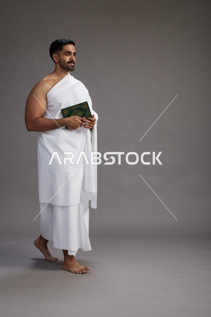 بورتريه لرجل سعودي بملابس الإحرام يقرأ القرآن أثناء الحج,  الجسم بالطول الكامل ,خلفيه رماديه