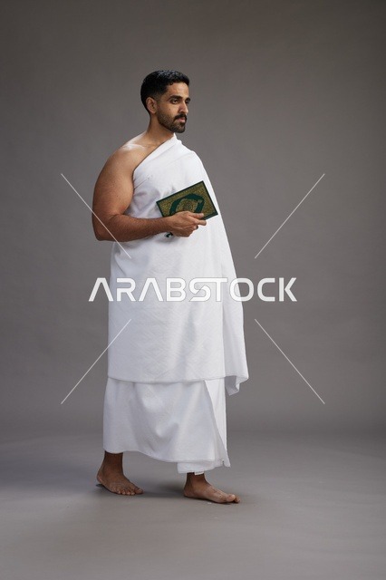 بورتريه لرجل سعودي بملابس الإحرام يقرأ القرآن أثناء الحج,  الجسم بالطول الكامل ,خلفيه رماديه