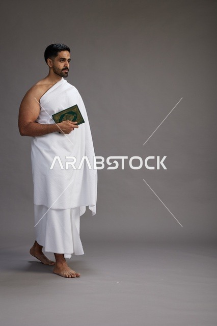 بورتريه لرجل سعودي بملابس الإحرام يقرأ القرآن أثناء الحج,  الجسم بالطول الكامل ,خلفيه رماديه