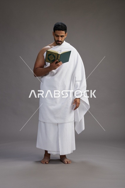 بورتريه لرجل سعودي بملابس الإحرام يقرأ القرآن أثناء الحج,  الجسم بالطول الكامل ,خلفيه رماديه