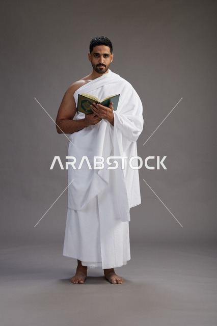 بورتريه لرجل سعودي بملابس الإحرام يقرأ القرآن أثناء الحج,  الجسم بالطول الكامل ,خلفيه رماديه