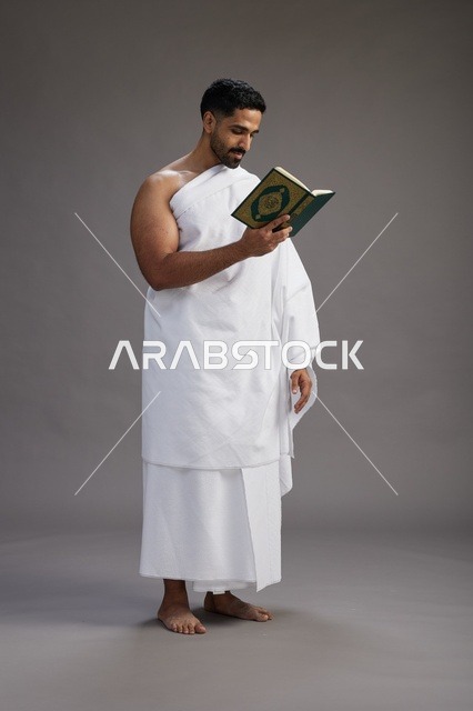 بورتريه لرجل سعودي بملابس الإحرام يقرأ القرآن أثناء الحج,  الجسم بالطول الكامل ,خلفيه رماديه