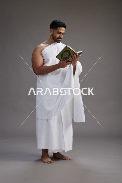 بورتريه لرجل سعودي بملابس الإحرام يقرأ القرآن أثناء الحج,  الجسم بالطول الكامل ,خلفيه رماديه