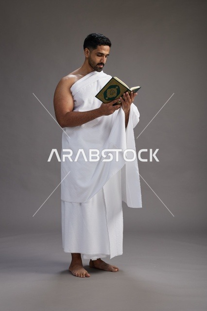 بورتريه لرجل سعودي بملابس الإحرام يقرأ القرآن أثناء الحج,  الجسم بالطول الكامل ,خلفيه رماديه