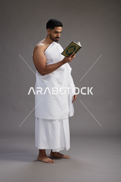 بورتريه لرجل سعودي بملابس الإحرام يقرأ القرآن أثناء الحج,  الجسم بالطول الكامل ,خلفيه رماديه