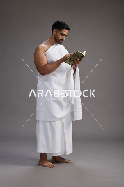 بورتريه لرجل سعودي بملابس الإحرام يقرأ القرآن أثناء الحج,  الجسم بالطول الكامل ,خلفيه رماديه