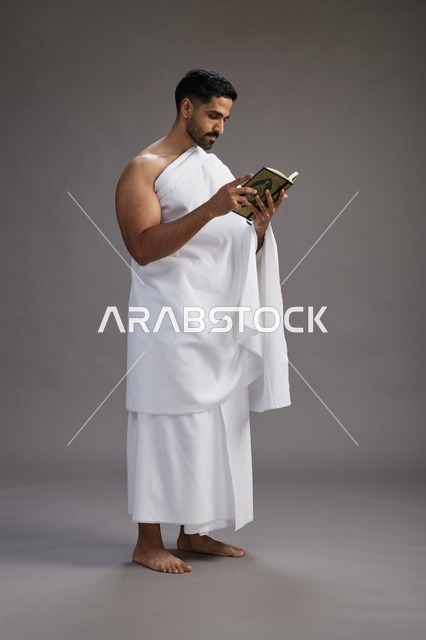 بورتريه لرجل سعودي بملابس الإحرام يقرأ القرآن أثناء الحج,  الجسم بالطول الكامل ,خلفيه رماديه