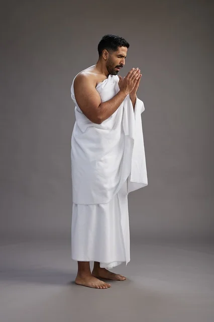 بورتريه لرجل سعودي بملابس الإحرام يعطس ويغطي فمه باحترام, مفهوم الحج والعمره, الجسم بالطول الكامل, خلفيه رماديه