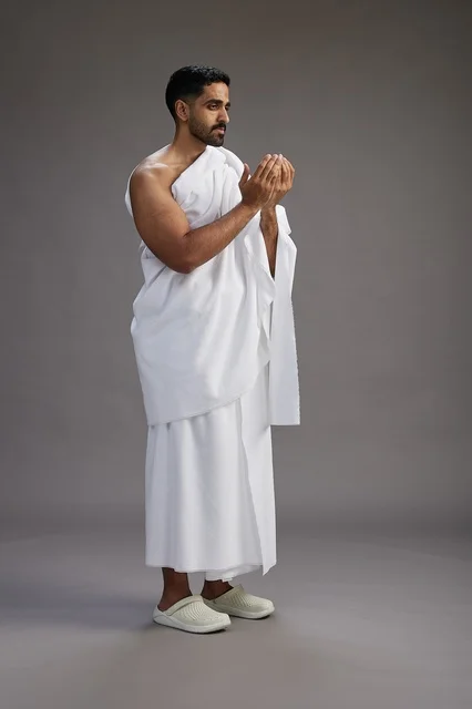 بورتريه لرجل سعودي بملابس الإحرام يدعو رافعاً يديه, الدعاء والتضرع لله , كامل الجسم, خلفيه رماديه