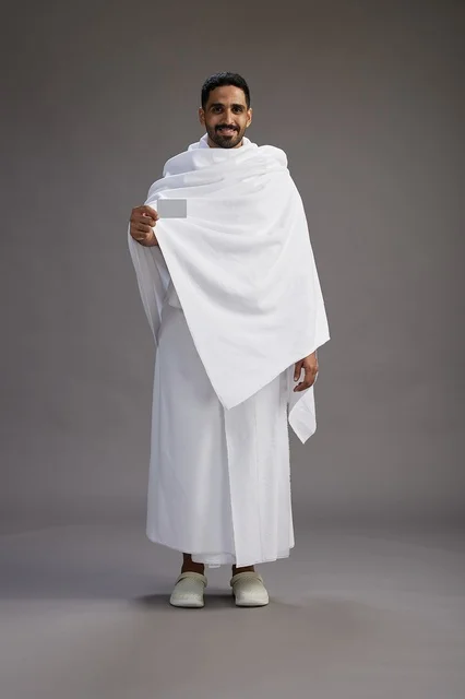 A portrait of a Saudi man in Ihram clothing holding a blank white card, representing the concepts of Hajj and Umrah, full body, gray background.