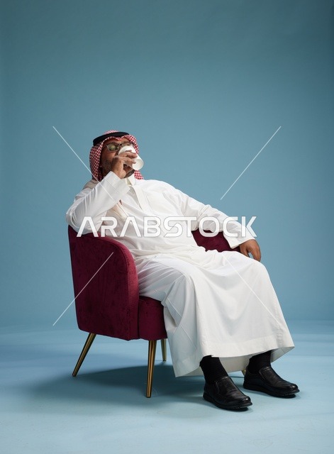 A portrait of an Arab Saudi Gulf man in a white thobe sitting holding a cup of coffee, enjoying hot beverages, with a blue background.