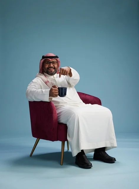 A portrait of an Arab Saudi Gulf man in a white thobe sitting holding a cup of coffee, enjoying hot beverages, with a blue background.
