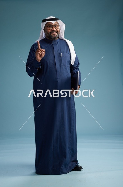 بورتريه لرجل سعودي بثوب أزرق وغترة بيضاء يستخدم الكمبيوتر المحمول, خلفيه زرقاء