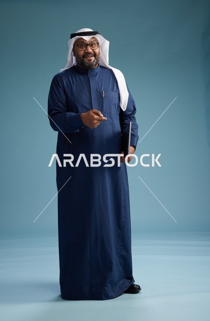 بورتريه لرجل سعودي بثوب أزرق وغترة بيضاء يستخدم الكمبيوتر المحمول, خلفيه زرقاء