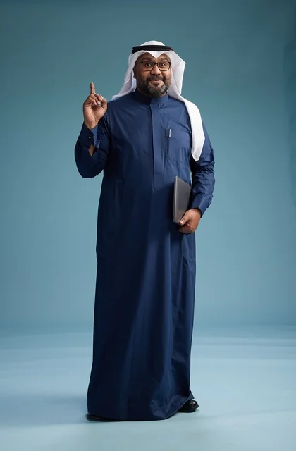 بورتريه لرجل سعودي بثوب أزرق وغترة بيضاء يستخدم الكمبيوتر المحمول, خلفيه زرقاء