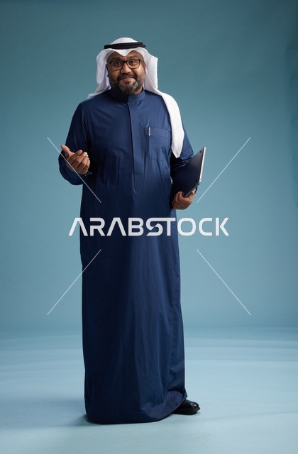 بورتريه لرجل سعودي بثوب أزرق وغترة بيضاء يستخدم الكمبيوتر المحمول, خلفيه زرقاء