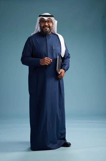 A portrait of a Saudi man in a blue thobe and white ghutrah using a laptop, with a blue background.