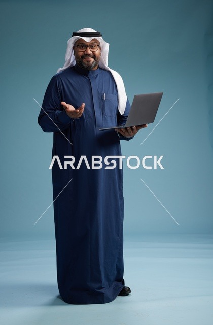 بورتريه لرجل سعودي بثوب أزرق وغترة بيضاء يستخدم الكمبيوتر المحمول, خلفيه زرقاء