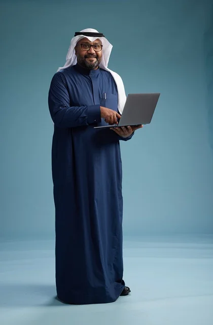 بورتريه لرجل سعودي بثوب أزرق وغترة بيضاء يستخدم الكمبيوتر المحمول, خلفيه زرقاء