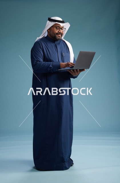 بورتريه لرجل سعودي بثوب أزرق وغترة بيضاء يستخدم الكمبيوتر المحمول, خلفيه زرقاء