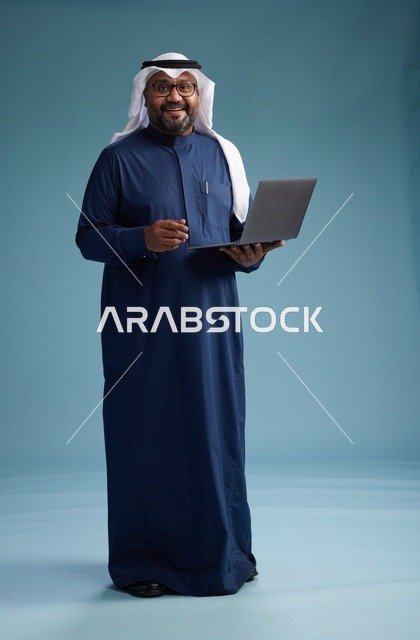 بورتريه لرجل سعودي بثوب أزرق وغترة بيضاء يستخدم الكمبيوتر المحمول, خلفيه زرقاء