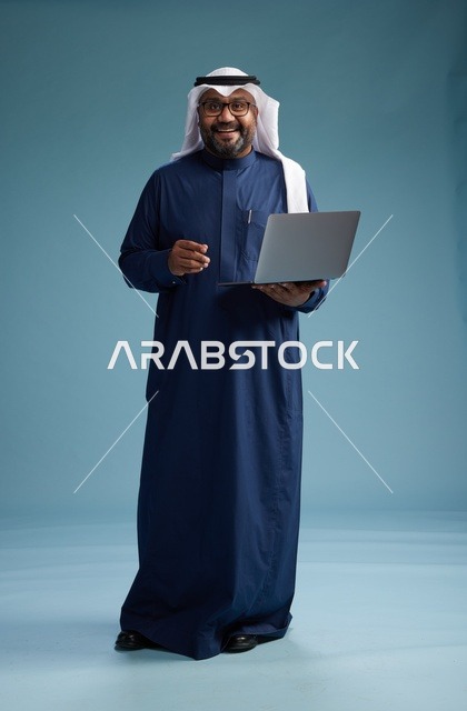 بورتريه لرجل سعودي بثوب أزرق وغترة بيضاء يستخدم الكمبيوتر المحمول, خلفيه زرقاء