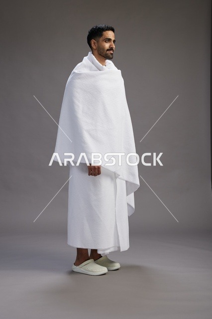 بورتريه لرجل عربي سعودي خليجي يرتدي ملابس الإحرام لأداء مناسك الحج, العباده والتقرب الى الله , الحج والعمره في مكه, الجسم بالطول الكامل , خلفيه رماديه