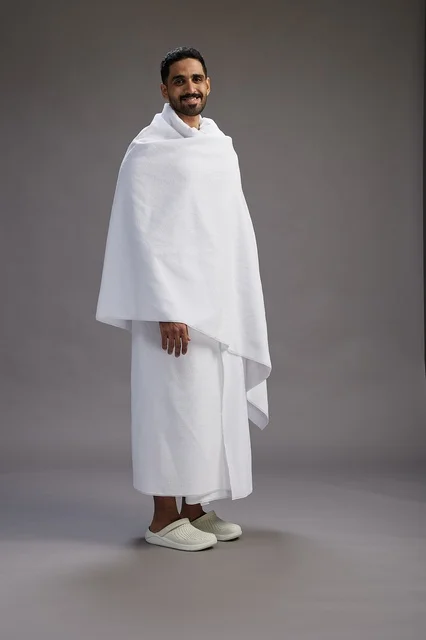 بورتريه لرجل عربي سعودي خليجي يرتدي ملابس الإحرام لأداء مناسك الحج, العباده والتقرب الى الله , الحج والعمره في مكه, الجسم بالطول الكامل , خلفيه رماديه
