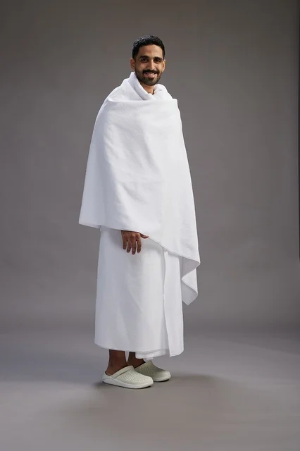 A portrait of an Arab Saudi Gulf man wearing Ihram clothing to perform the rituals of Hajj, worship, and drawing closer to God, Hajj and Umrah in Mecca, full-body, gray background.