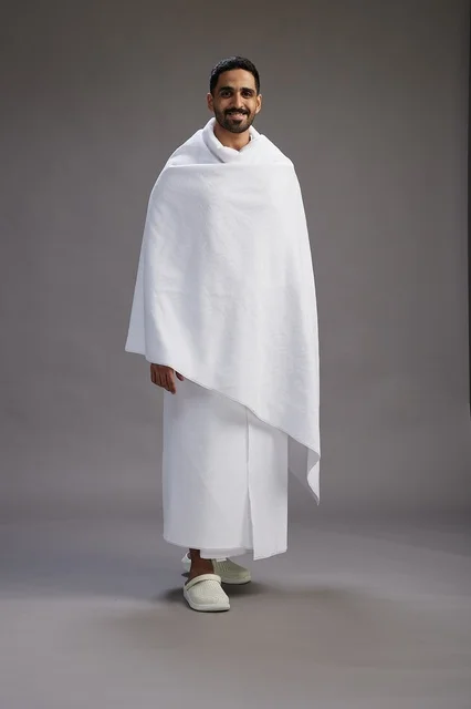 بورتريه لرجل عربي سعودي خليجي يرتدي ملابس الإحرام لأداء مناسك الحج, العباده والتقرب الى الله , الحج والعمره في مكه, الجسم بالطول الكامل , خلفيه رماديه