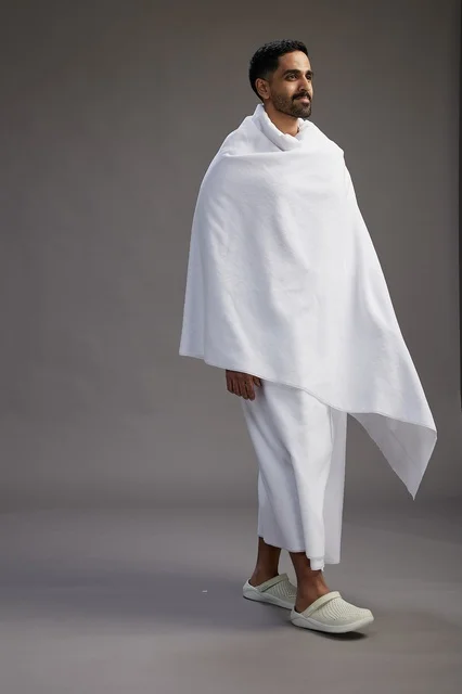 بورتريه لرجل عربي سعودي خليجي يرتدي ملابس الإحرام لأداء مناسك الحج, العباده والتقرب الى الله , الحج والعمره في مكه, الجسم بالطول الكامل , خلفيه رماديه