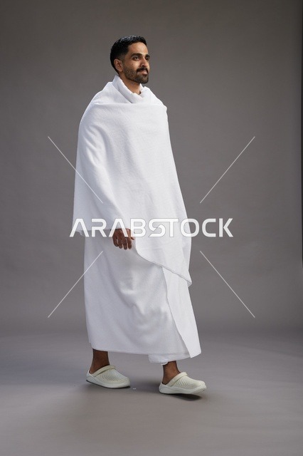 بورتريه لرجل عربي سعودي خليجي يرتدي ملابس الإحرام لأداء مناسك الحج, العباده والتقرب الى الله , الحج والعمره في مكه, الجسم بالطول الكامل , خلفيه رماديه